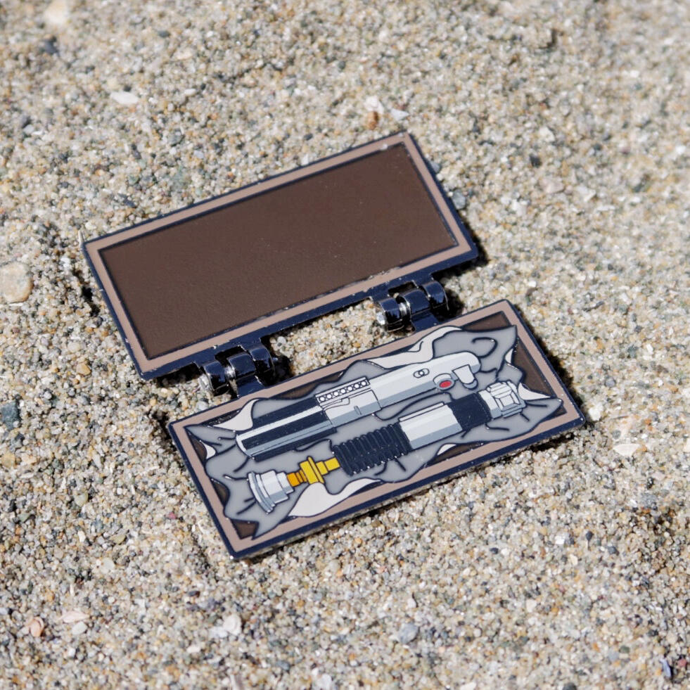 Hinged enamel pin made to look like a wooden box, with Obi-Wan and Anakin’s lightsaber hilts inside.